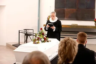 En præst står ved i pyntet kiste i en kirke